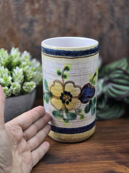 Vintage Keramikvase mit gelber Blüte, blauem Akzent und grünen Blättern, daneben eine Hand zur Größenorientierung.