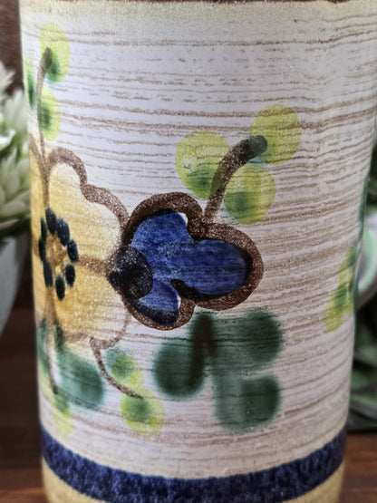 Detailansicht der Vintage Keramikvase mit beigefarbenem Grund, grünen Blättern, blauem Blütendetail und sichtbarer Glasurstruktur.