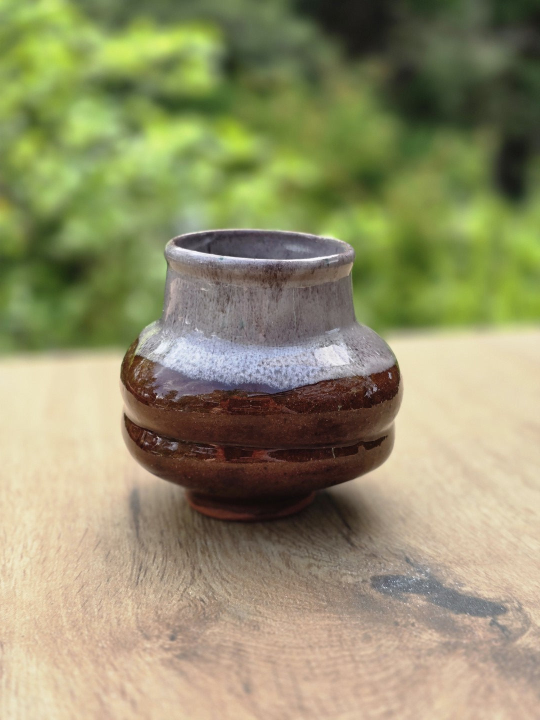Kleine bauchige Keramikvase mit brauner Laufglasur, grauem Hals und glänzender Oberfläche auf einem Holztisch