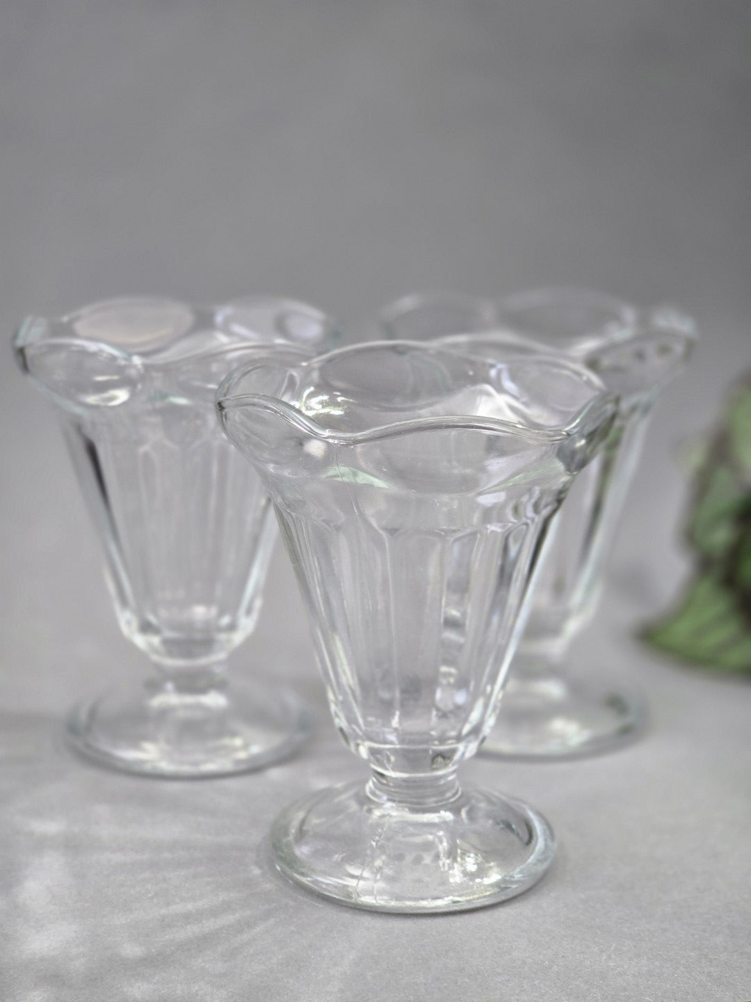Mehrere transparente Eisbecher stehen auf grauem Untergrund, vorne ist ein klarer Glasbecher mit gewelltem Rand und geripptem Kelch zu sehen