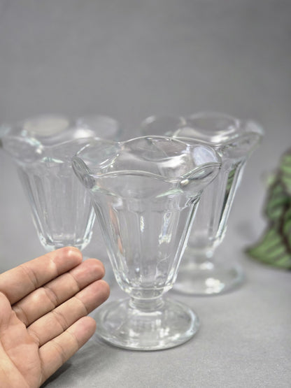 Ein transparenter Eisbecher steht im Vordergrund, dahinter sind zwei weitere Gläser unscharf zu sehen, links dient eine Hand als Größenvergleich
