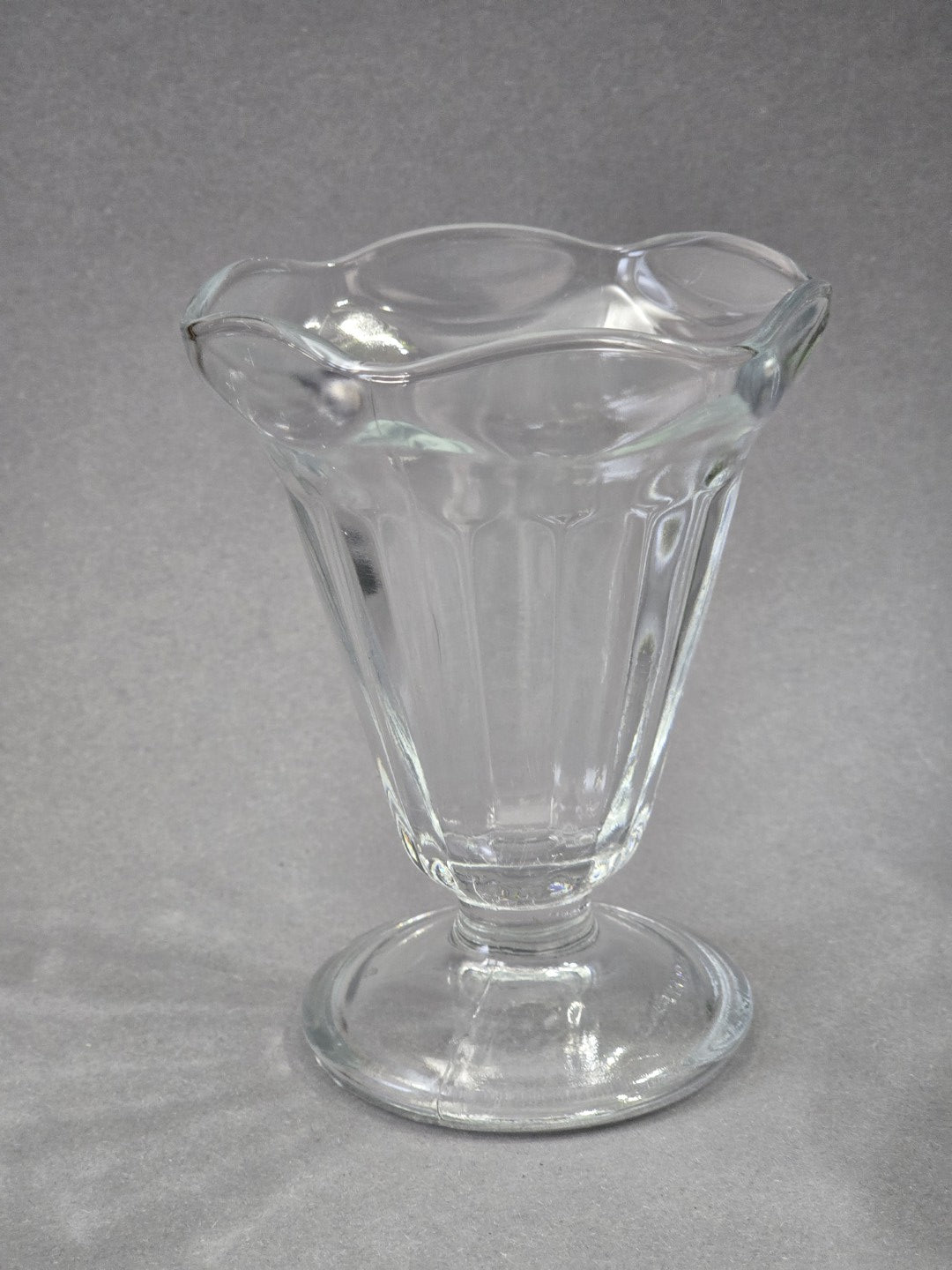 Einzelner klarer Glasbecher von vorne, mit tulpenförmiger Öffnung, senkrechten Rippen im Kelch und rundem Standfuß