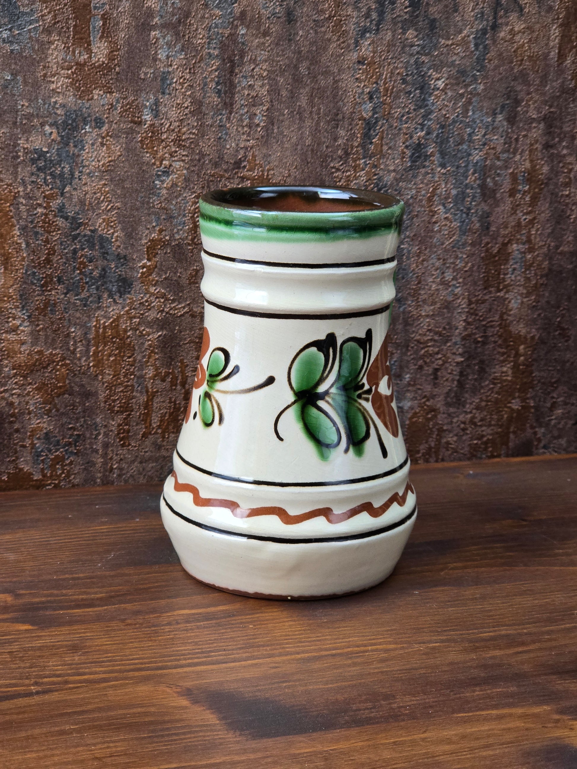 Vintage Henkelkrug mit handwerklicher Ausstrahlung, floralem Dekor in Grün und Braun, heller Cremeglasur und rotbrennendem Boden.
