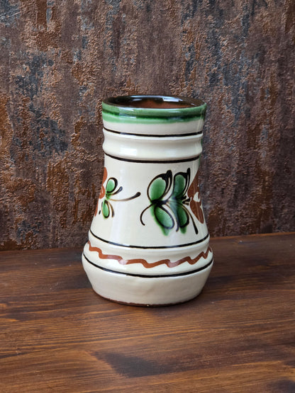 Vintage Henkelkrug mit handwerklicher Ausstrahlung, floralem Dekor in Grün und Braun, heller Cremeglasur und rotbrennendem Boden.