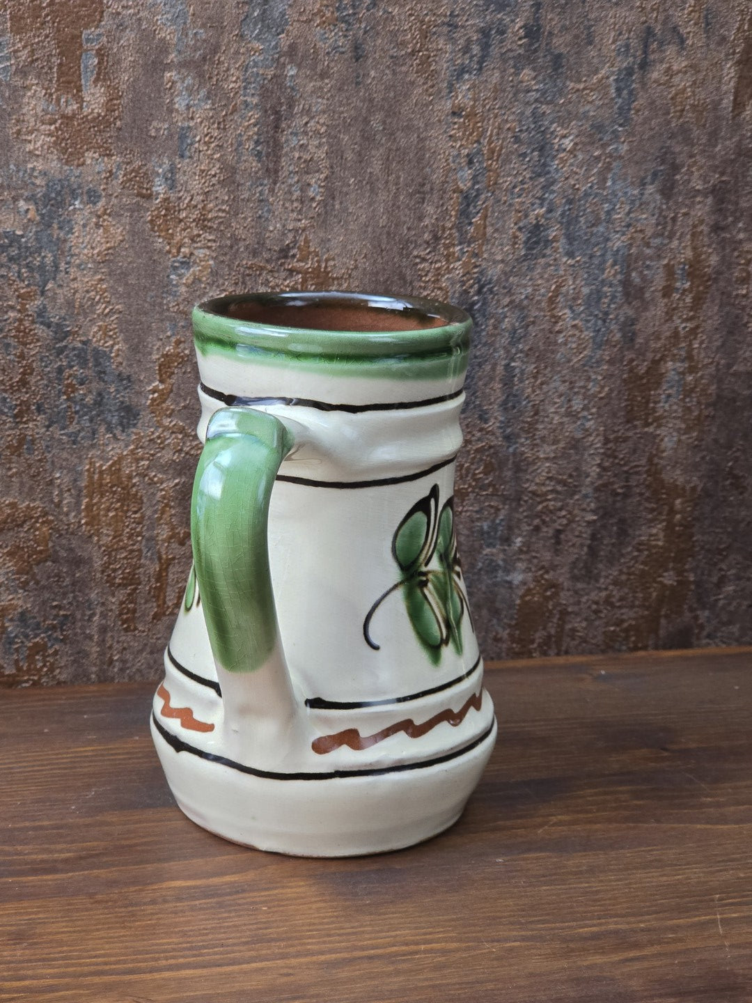 Dekorativer Henkelkrug aus Vintage-Keramik mit Blumenmotiv in Grün und Braun, cremefarbener Glasur und rotbrennendem Keramikboden.