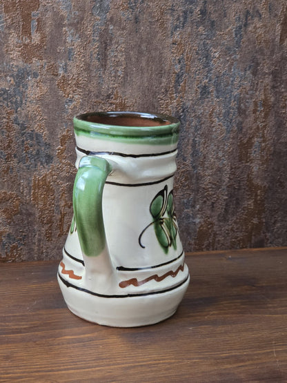 Dekorativer Henkelkrug aus Vintage-Keramik mit Blumenmotiv in Grün und Braun, cremefarbener Glasur und rotbrennendem Keramikboden.