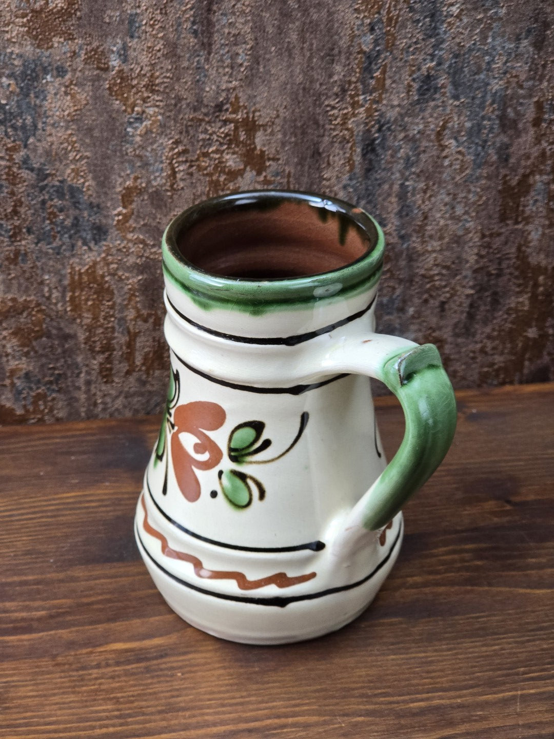 Vintage Keramik Krug mit handwerklichem Charakter, grünem Henkel, hellem cremefarbenem Glasurton und floralem Dekor in Braun und Grün.