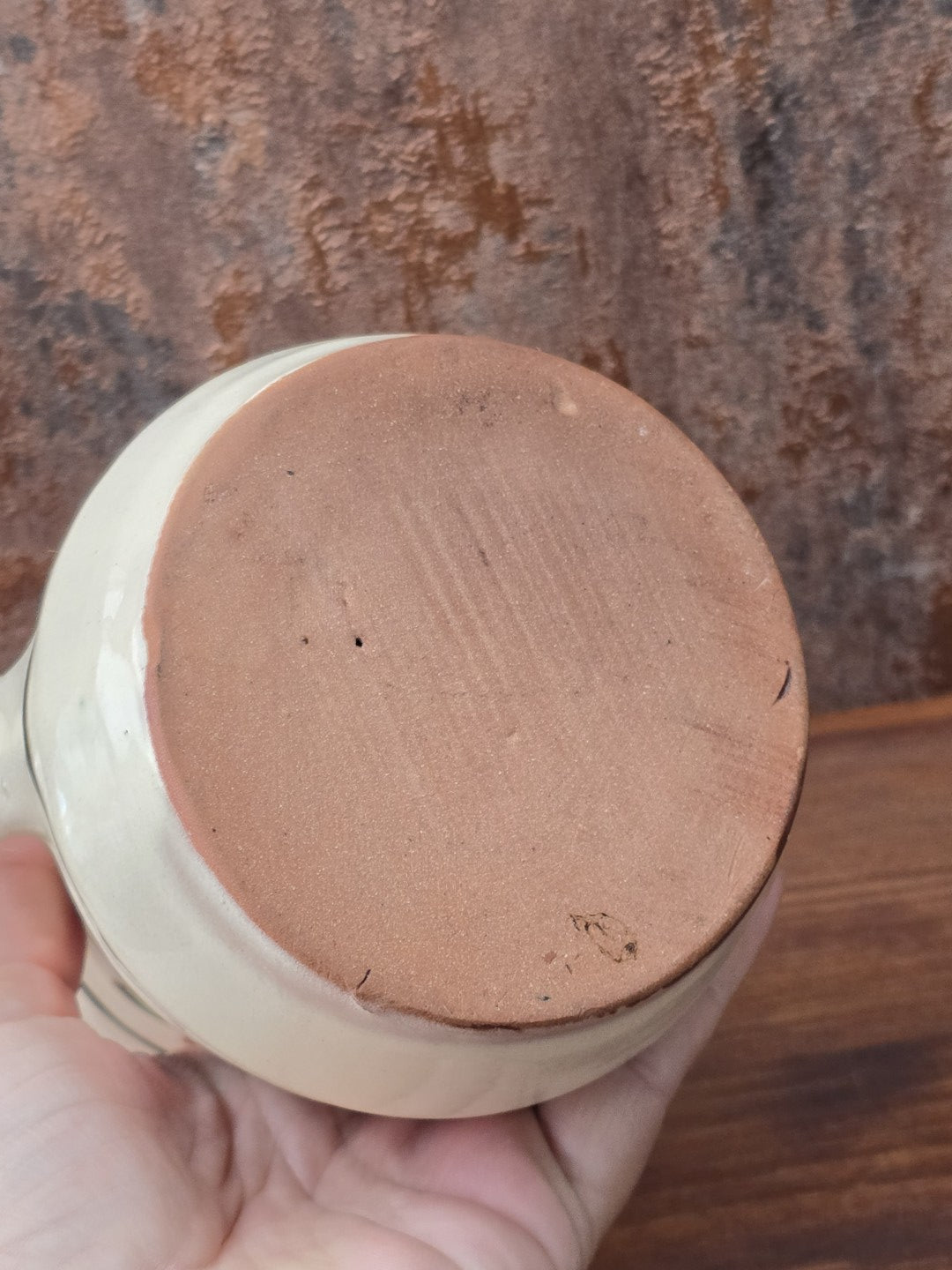 Rustikaler Keramik Krug im Vintage-Stil mit grünem Henkel, floralem Dekor in Braun und Grün, cremefarbener Glasur und sichtbarem Terrakotta-Boden.
