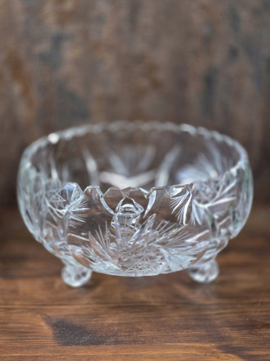 Vintage Kristallglasschale auf drei Füßen mit facettiertem Rand und floralem Sternschliff, frontal auf dunkler Holzfläche fotografiert.