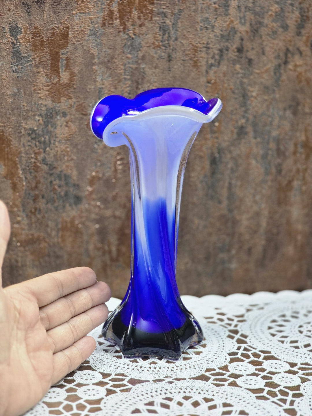 Glasvase mit blau-weißem Farbverlauf, geschwungenem Rand und klarem Fuß, neben einer Hand als Größenvergleich