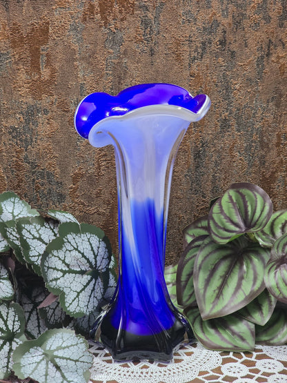 Glasvase mit blauem und weißem Glas, wellenförmigem Rand und glänzender Oberfläche vor strukturierter Wand