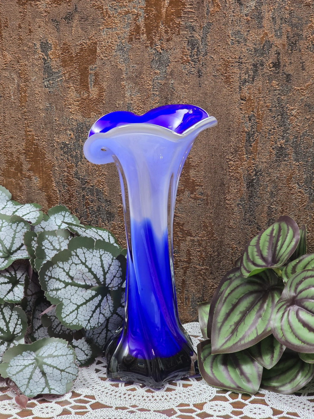 Glasvase mit gewelltem blauem Rand, milchweißem Hals und kobaltblauem Verlauf zwischen Blattpflanzen