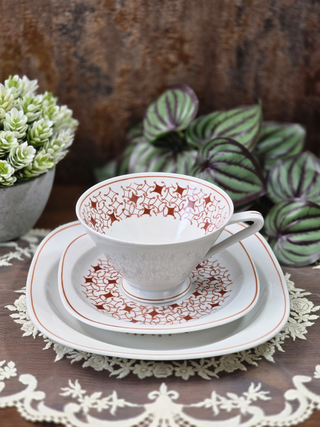 Vintage Kaffeegedeck aus weißem Porzellan mit Tasse, Untertasse, Kuchenteller und braunrotem Muster auf Spitzendecke