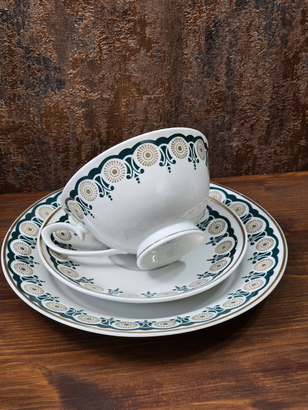 Vintage Lettin Porzellangedeck mit schräg liegender Tasse, grün-goldenem Dekor und Goldlinien auf Holztisch