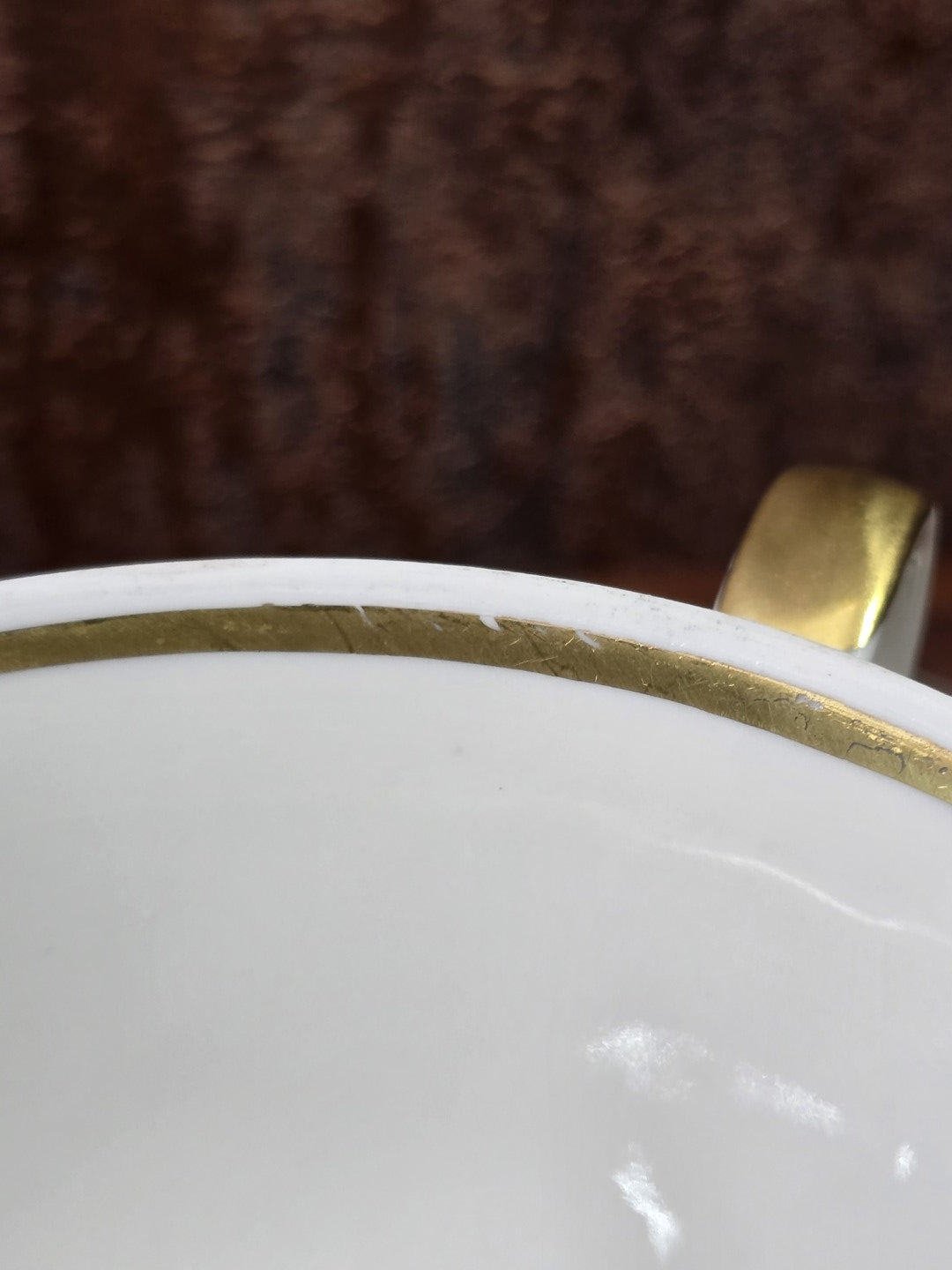 Vintage Porzellantasse mit Goldrand und vergoldetem Henkel, Detailaufnahme des Innenrands vor dunklem Hintergrund