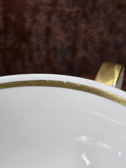 Vintage Porzellantasse mit Goldrand und vergoldetem Henkel, Detailaufnahme des Innenrands vor dunklem Hintergrund