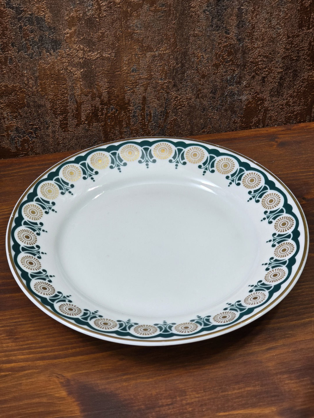 Vintage Porzellanteller mit grün-goldenem Ornamentrand und weißer Mitte auf Holztisch in schräger Draufsicht