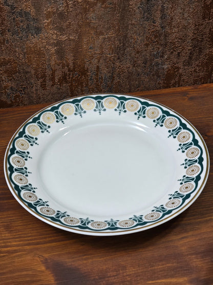 Vintage Porzellanteller mit grün-goldenem Ornamentrand und weißer Mitte auf Holztisch in schräger Draufsicht