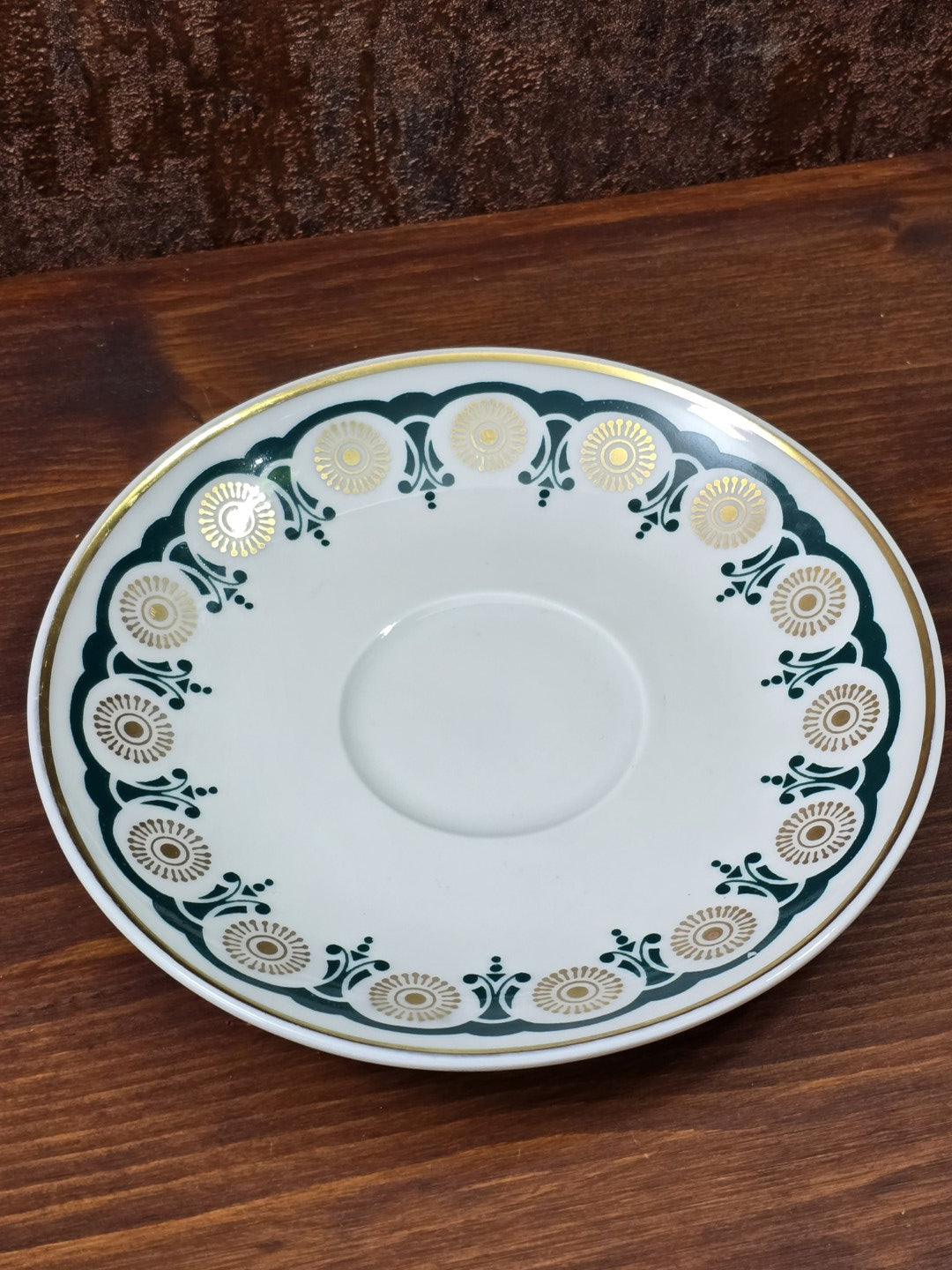 Vintage Porzellanuntertasse mit grün-goldenem Randdekor, Goldlinie und Tassenvertiefung auf Holztisch