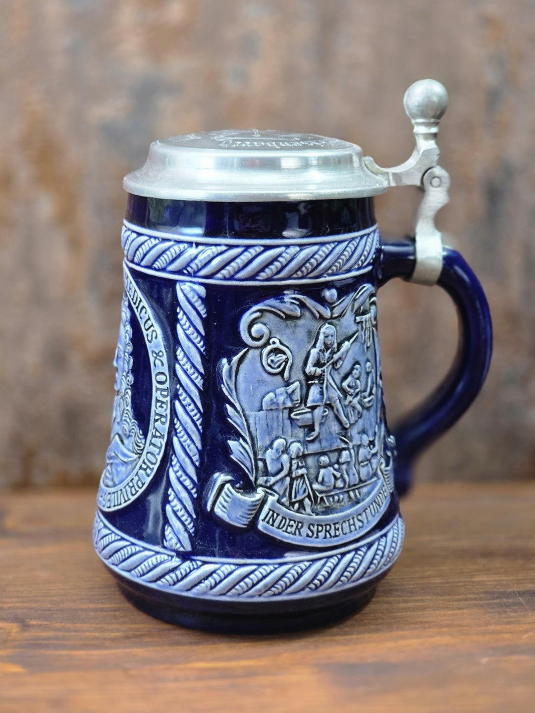 Vintage Marzi & Remy Bierkrug aus kobaltblauem Steinzeug mit Zinndeckel und Reliefszene „In der Sprechstunde“ in Frontalansicht.