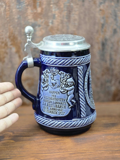 Vintage Doktor-Eisenbarth-Krug aus blauem Steinzeug mit Wappenrelief, Zinndeckel und Hand daneben zur Darstellung der Größe.
