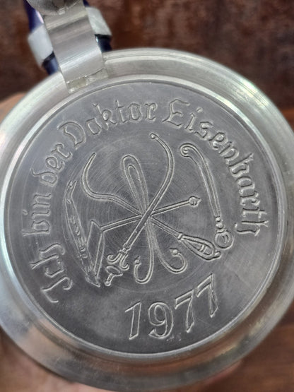 Vintage Bierkrug mit Zinndeckel in Nahaufnahme, graviert mit „Zur Erinnerung an den Doktor Eisenbarth“ und der Jahreszahl 1977.