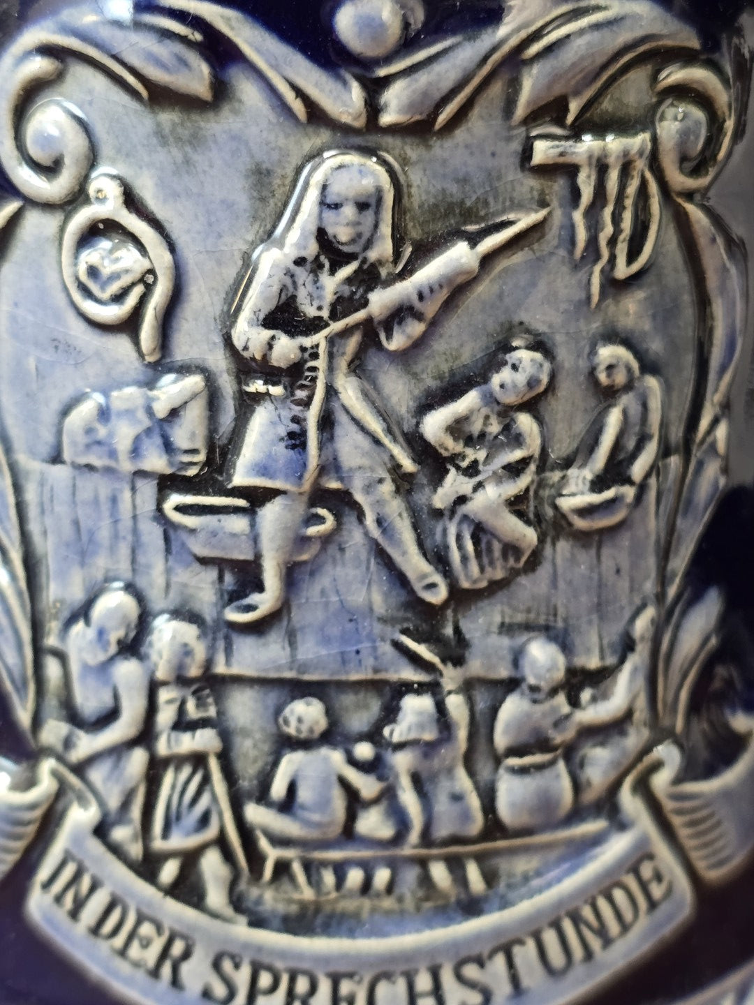 Vintage Doktor-Eisenbarth-Krug mit plastischer Sprechstunden-Szene, mehreren Figuren und Schriftband „In der Sprechstunde“ im Detail.