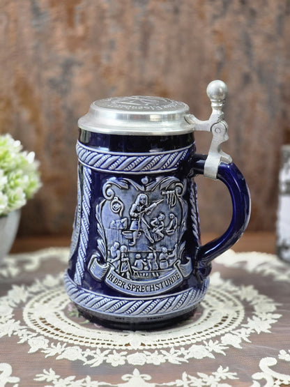 Vintage Doktor-Eisenbarth-Bierkrug mit kobaltblauer Glasur, Zinndeckel und Reliefszene „In der Sprechstunde“ auf Spitzendecke.