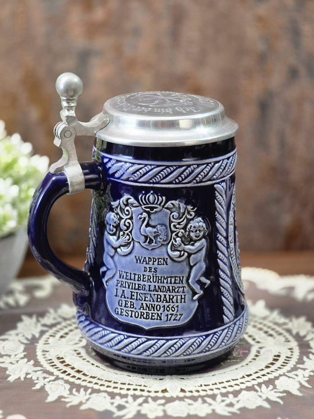 Vintage Marzi & Remy Bierkrug mit Zinndeckel, blauem Henkel und Wappenrelief zu Johann Andreas Eisenbarth in frontaler Seitenansicht.