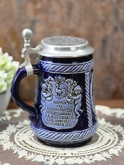 Vintage Marzi & Remy Bierkrug mit Zinndeckel, blauem Henkel und Wappenrelief zu Johann Andreas Eisenbarth in frontaler Seitenansicht.