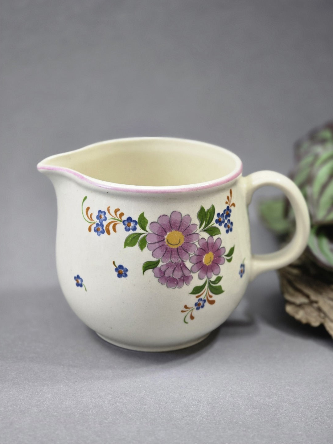 Helles Vintage Milchkännchen aus Keramik mit rosa Rand, rundem Henkel, Ausguss und floralem Dekor aus lila und blauen Blumen.