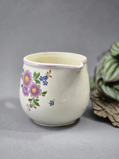 Bauchiges Vintage Milchkännchen mit Ausguss, rosa Randlinie und handlichem Henkel, dekoriert mit lila Blüten, blauen Blumen und grünen Blättern.
