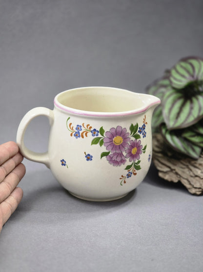 Vintage Keramik Milchkännchen mit Blumenmotiv und rosa Rand, neben einer Hand fotografiert, um Größe und Form besser zu zeigen.