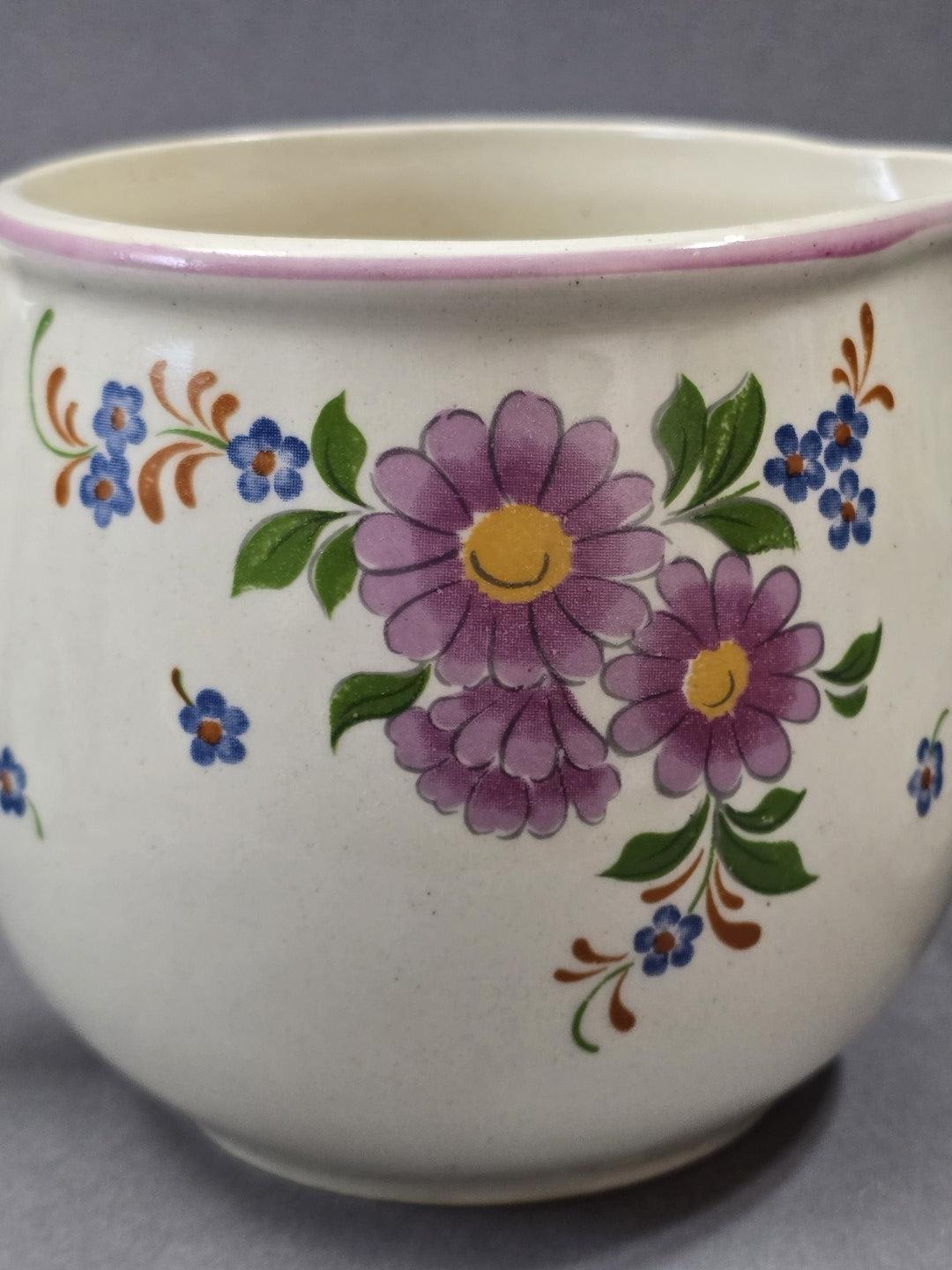 Detailaufnahme des floralen Dekors mit großen lila Blüten, gelber Mitte, kleinen blauen Blumen, grünen Blättern und rosa Randlinie.