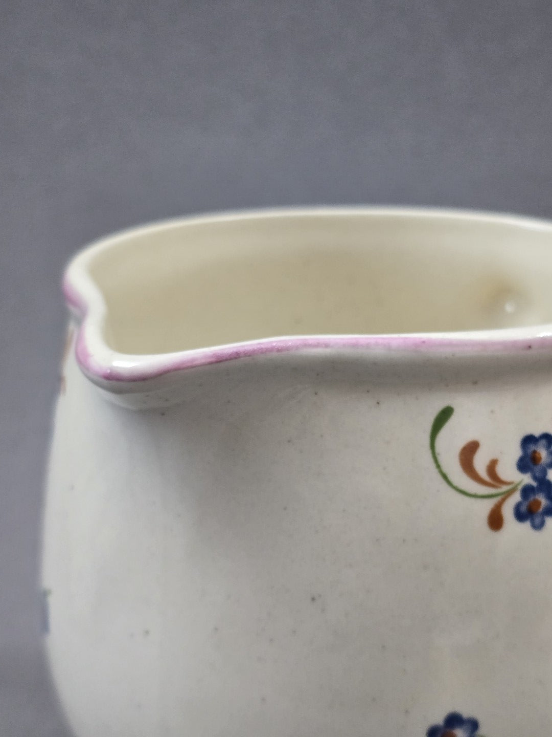 Detail des oberen Randes am Milchkännchen mit rosa Linie, hellem Innenraum, leicht geschwungenem Ausguss und feiner Glasurstruktur.