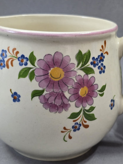 Florales Detail auf hellem Keramikkorpus mit lila Blüten, blauen Blumen, grünen Blättern und gelben Blütenmitten.