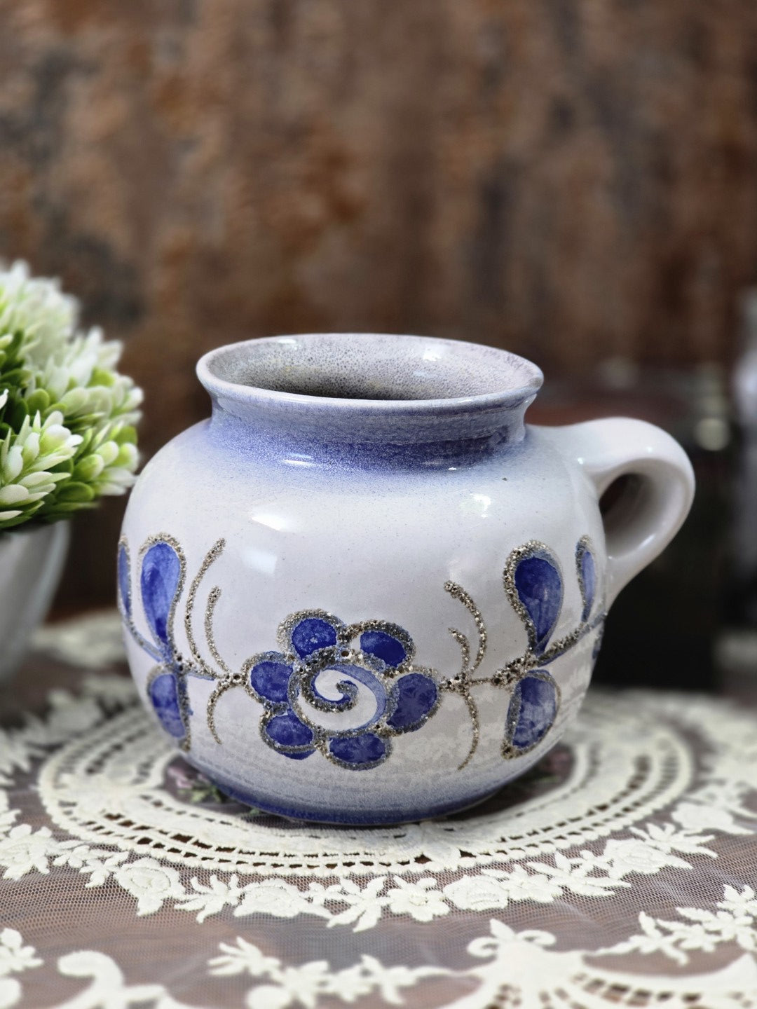 Vintage Strehla Henkelvase aus Keramik mit blauem floralem Dekor, heller Glasur und kurzem Henkel auf dekorativer Spitzendecke