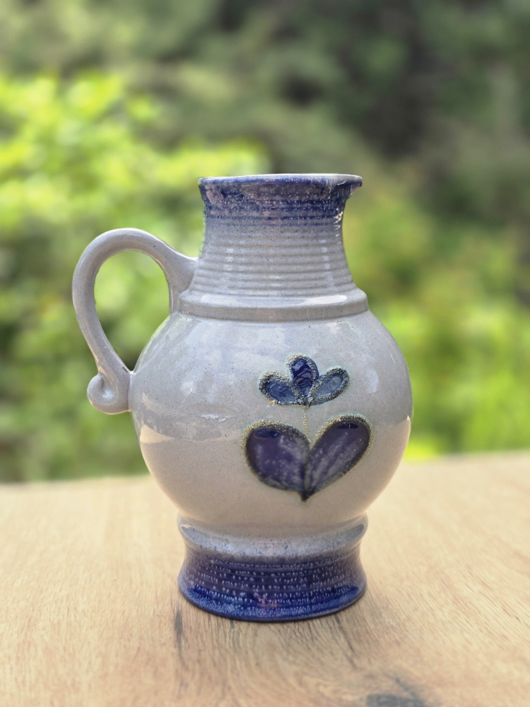 Vintage Keramikkrug mit Henkel, blauem Fuß, gerilltem Hals und violettblauem Blumendekor auf heller Glasur.
