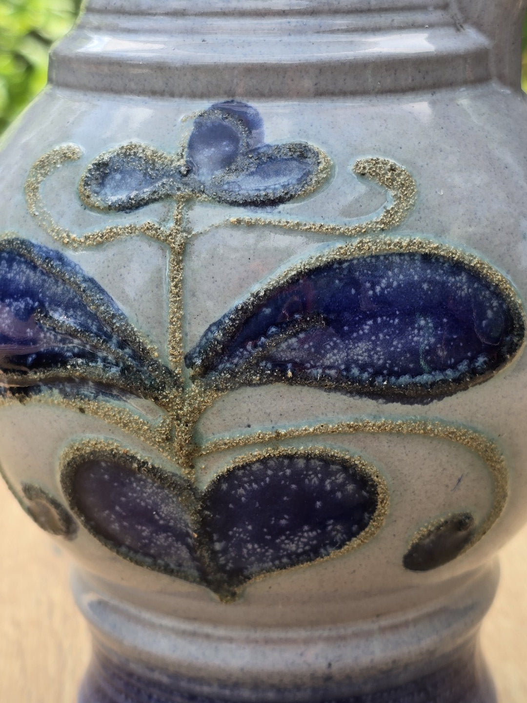 Nahaufnahme des violettblauen Blumendekors auf heller Glasur mit körniger Kontur und glänzender Keramikoberfläche.