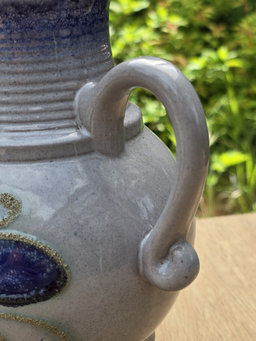 Detail des geschwungenen Henkels am hell glasierten Keramikkrug mit bauchiger Form und blauem Dekoransatz.