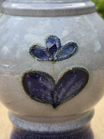 Kleines violettblaues Blütenmotiv auf heller Glasur, detailreich fotografiert auf der Vorderseite des Keramikkrugs.