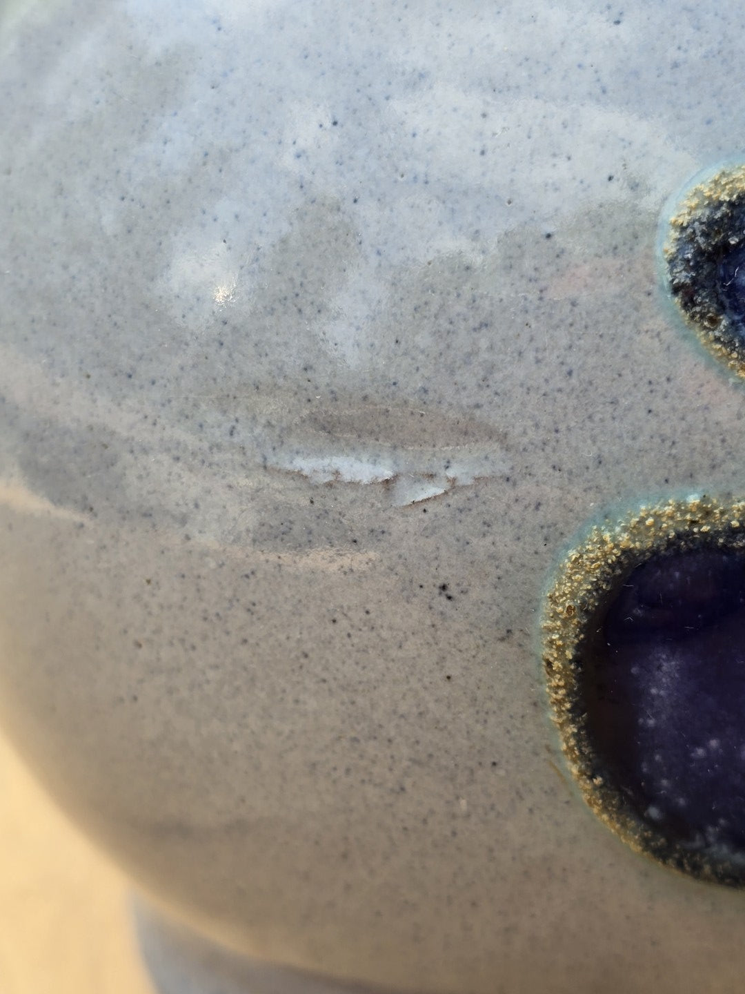 Detail der hellen Keramikglasur mit feinen Gebrauchsspuren und angeschnittenem violettblauem Dekor am Krug.