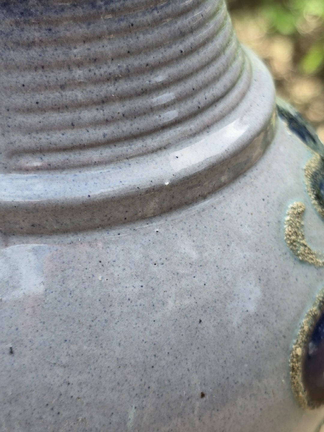 Detail der Schulterpartie des Keramikkrugs mit glänzender graublauer Glasur, feinen Sprenkeln und floralem Dekoransatz.