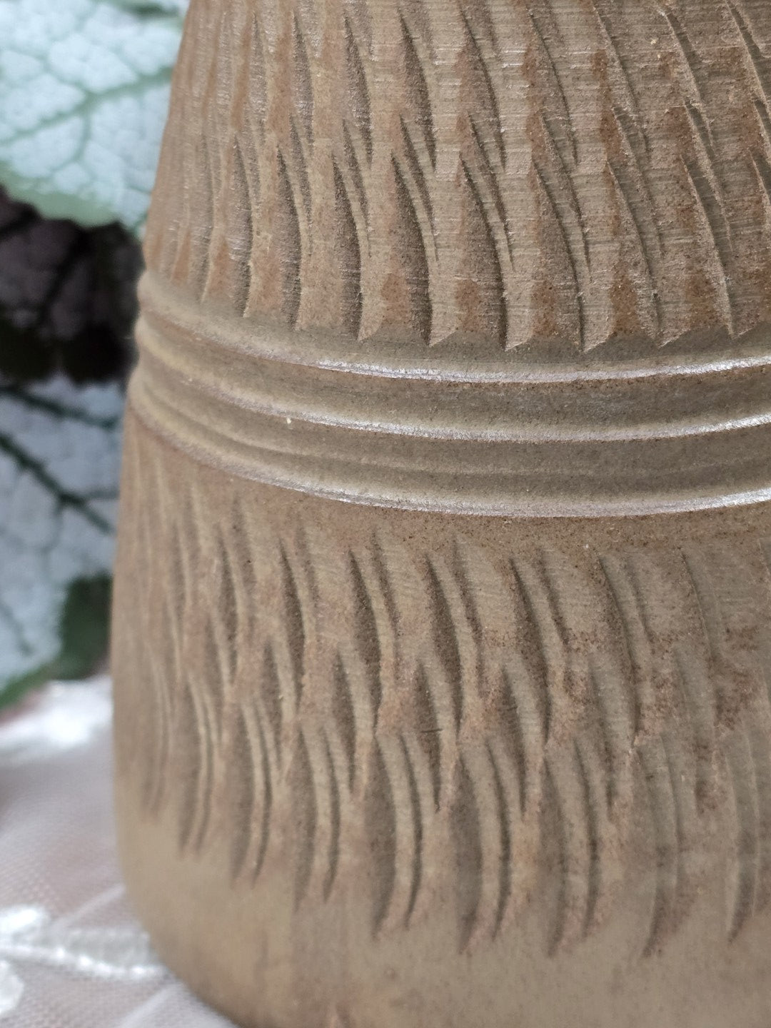 Keramikvase mit Kerbschnittmuster und Rillenbändern, neben einer Hand als Größenvergleich auf weißer Spitzendecke