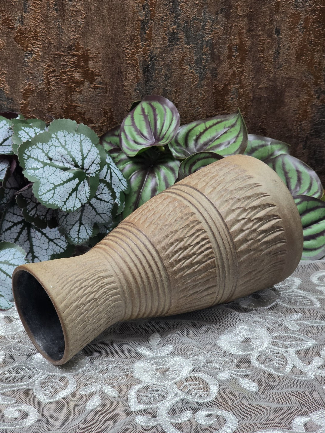 Keramikvase mit Kerbschnittdekor und glänzenden Rillenbändern in Nahaufnahme vor grün gemusterten Blättern