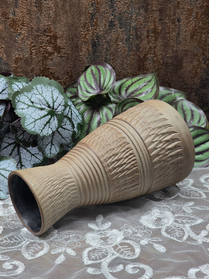 Keramikvase mit Kerbschnittdekor und glänzenden Rillenbändern in Nahaufnahme vor grün gemusterten Blättern