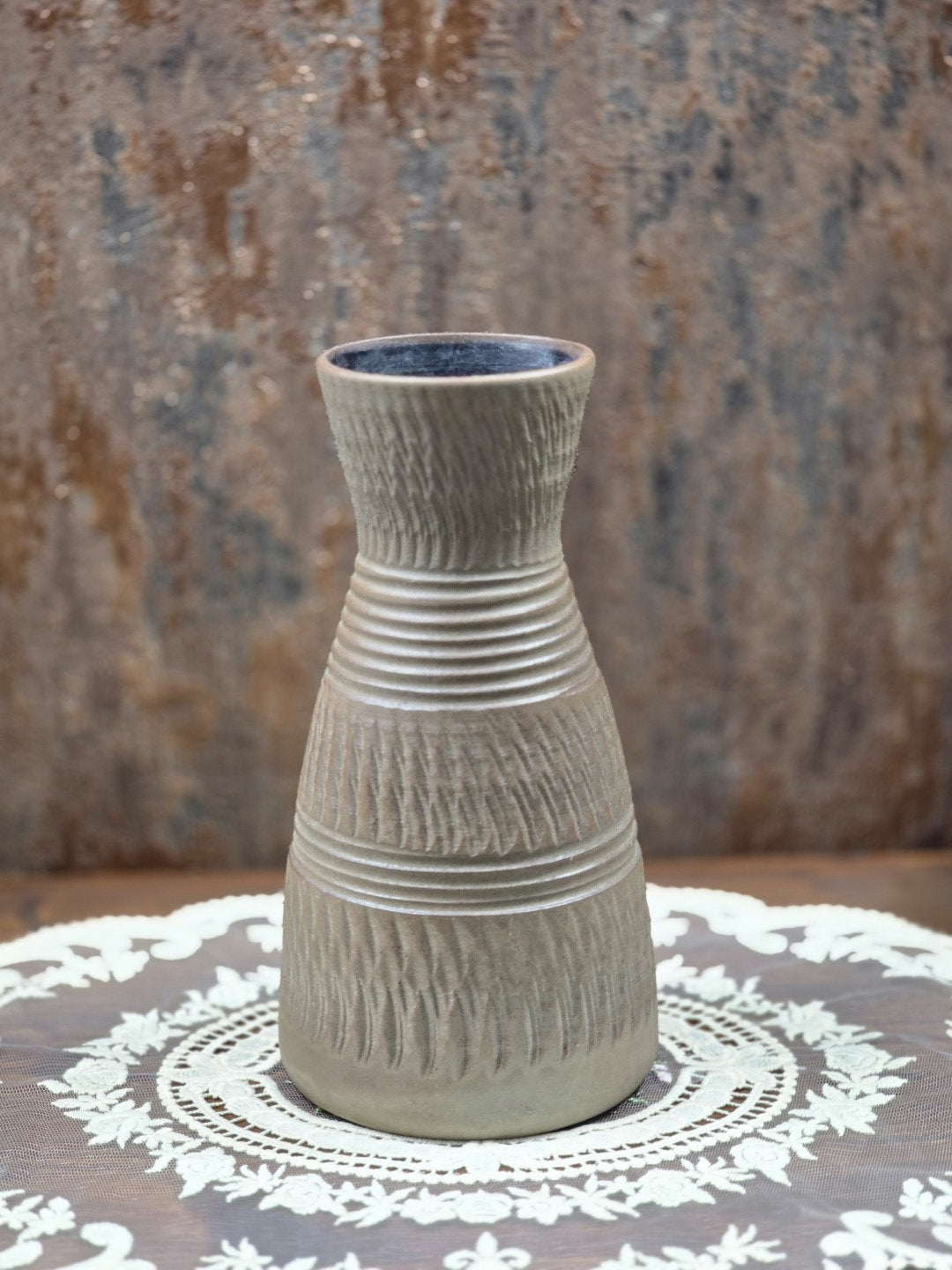 Keramikvase mit rosa Kunstblumen, braungrauer Oberfläche, Rillenbändern und Kerbschnittdekor zwischen Blattpflanzen