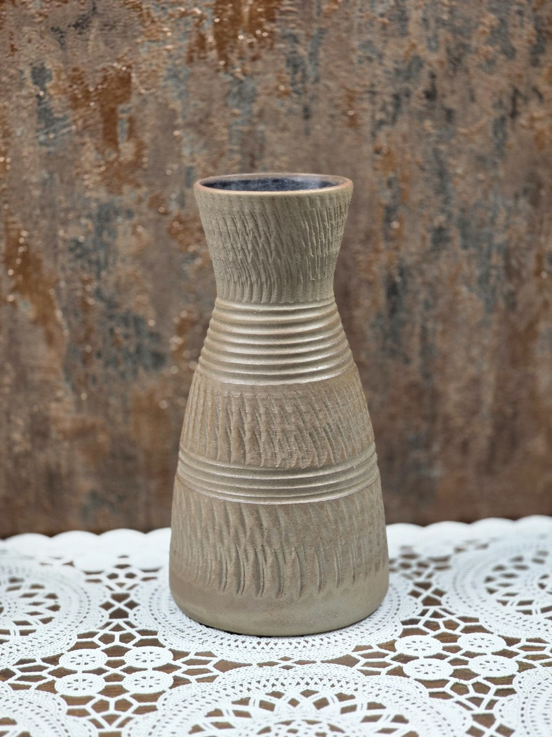 Keramikvase in Frontalansicht mit matter braungrauer Glasur, eingeritztem Dekor und Rillen auf Holztisch