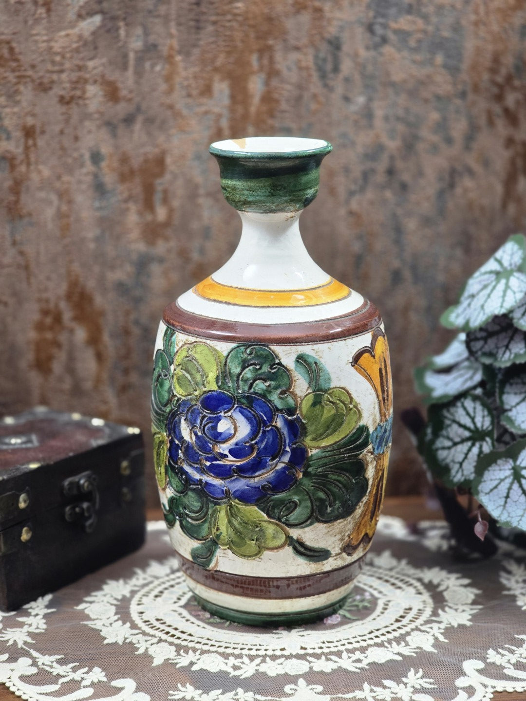 Keramikvase mit floralem Reliefdekor, blauer Blüte, grünen Blättern und braunen Zierbändern auf Spitzendecke
