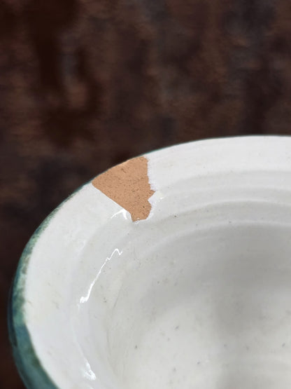 Keramikvase mit grünem Rand und sichtbarem Chip an der Mündung in enger Detailaufnahme